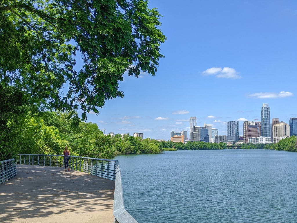 a view of downtown Austin from a lakefront platform with a tree shading i
