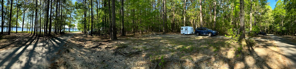 A small camper and a Subaru Ascent in a wooded campground.