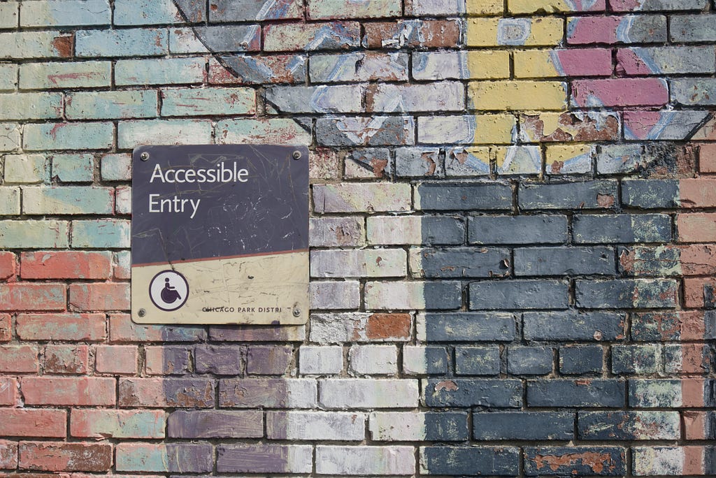 A colourful painted wall with a sign directing people to the accessible entry of a building.