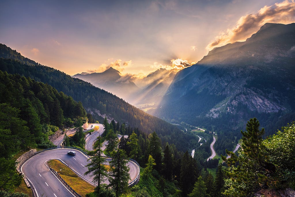 Image shows a scenic view of a winding road along mountains.