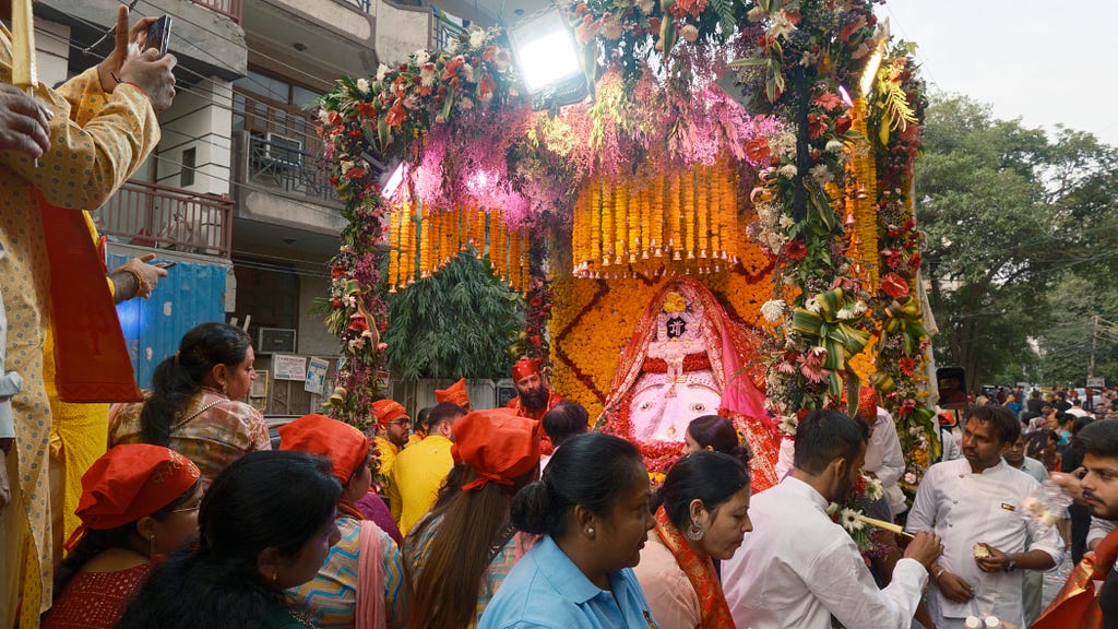 Hindu idol tableau with people sitting around it on a truck, passing through a street.