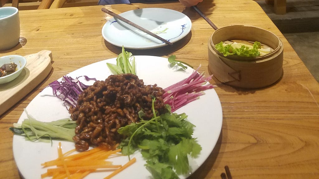 a plate of Beijing Roast Duck and fresh veggies on a wooden table