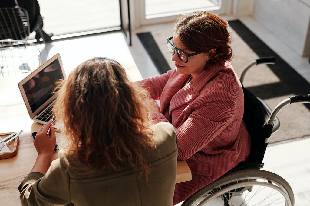 Two women having a conversation over a laptop. One of them is in a wheelchair.