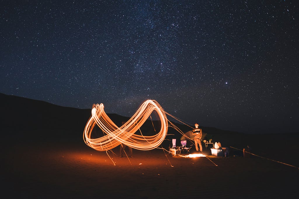 Man creating yellow infinity symbol with light standing in the darkness