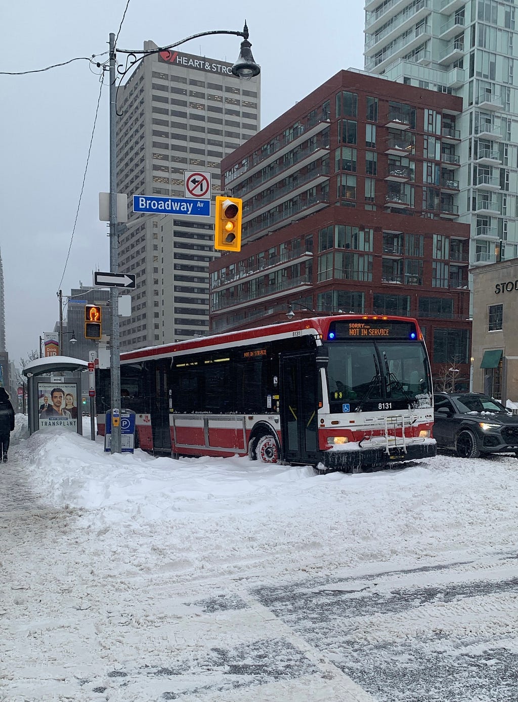 Toronto Transit Commission (TTC) bus stuck in snowbank at intersection of Broadway Avenue and Yonge Street.