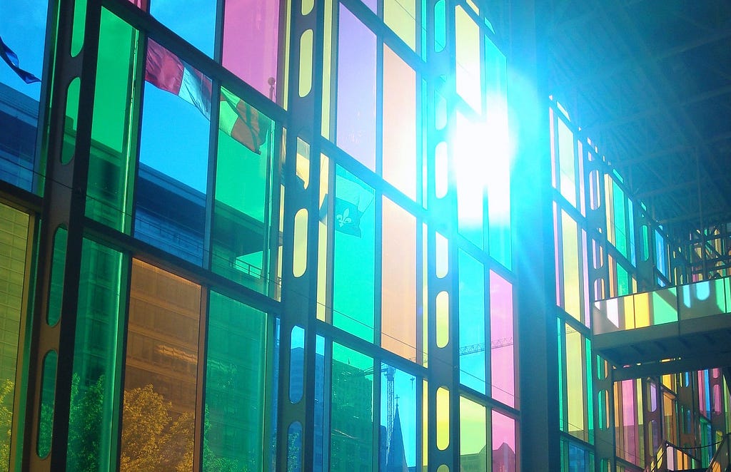 Multicolour stained glass with light shining through and Canadian flag on opposite side (photo by Kate Kalcevich)