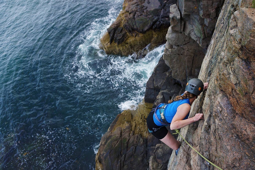 An American female traveler doing some rock climbing on a cliff on the coast with water underneath