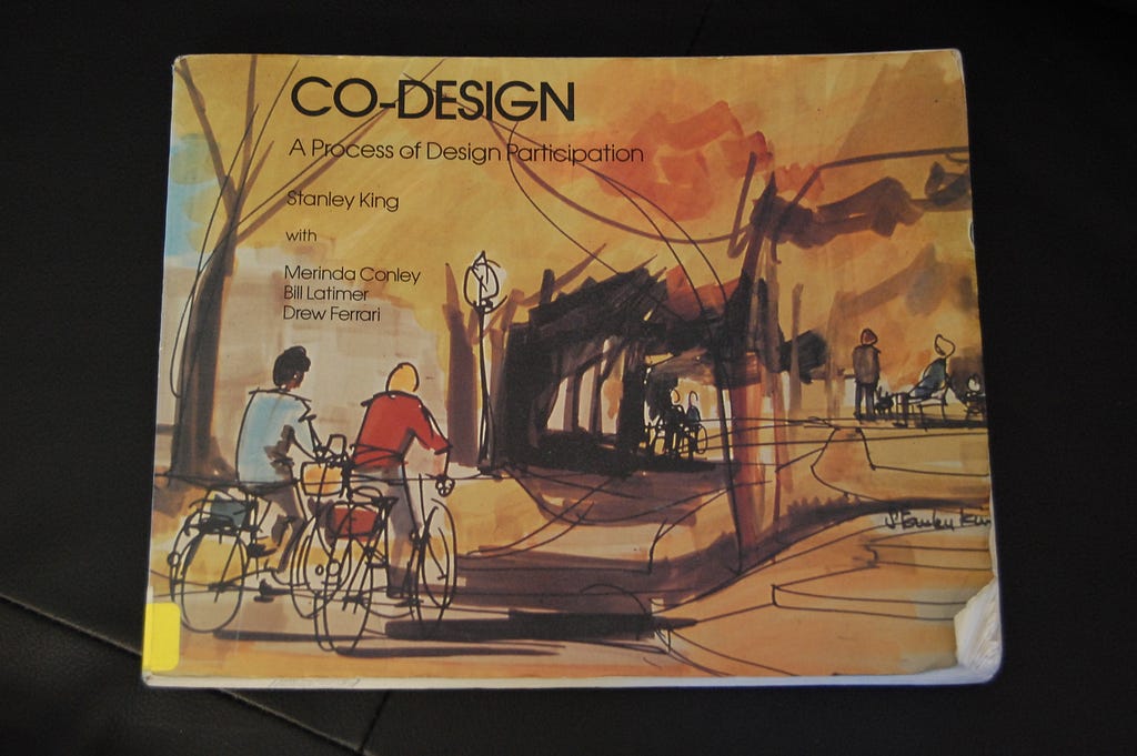 A picture of book that is golden in colour with illustration on it of two people cycling on bikes. The title says Co-Design