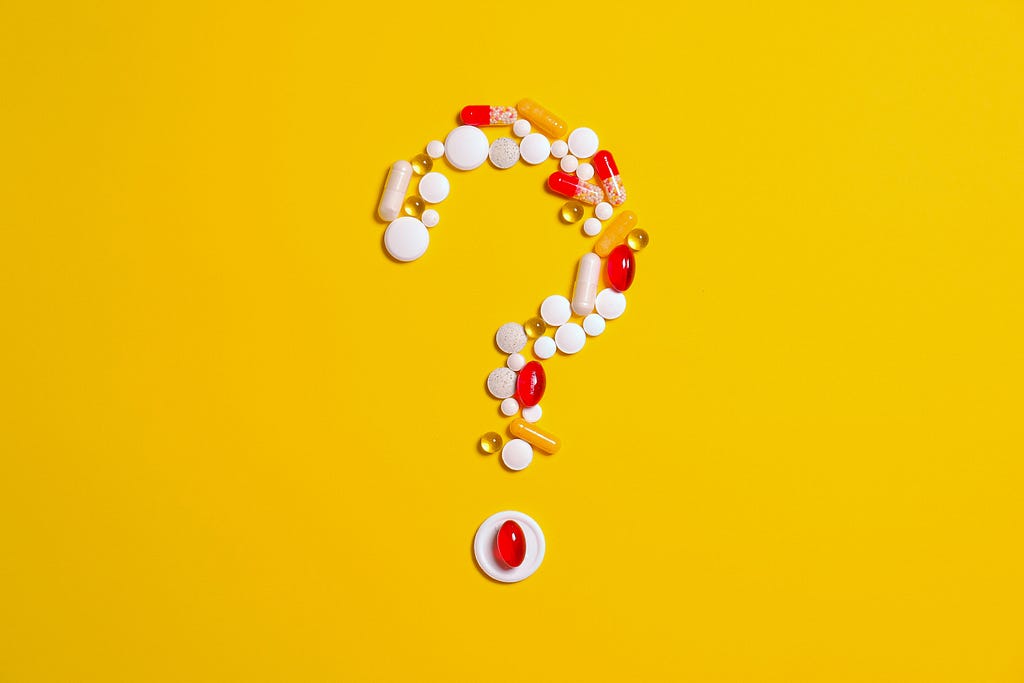 Question mark made out of different pills on a yellow background.