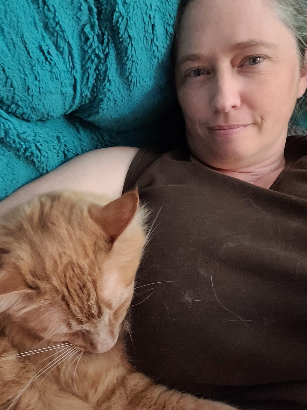 Woman laying on teal papasan with ginger cat snuggled at her side