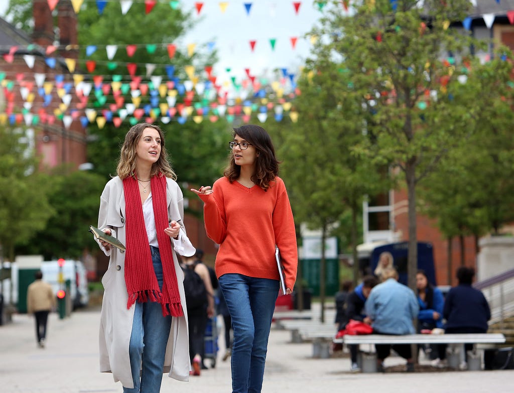 two students walking through campus, chatting to one another.