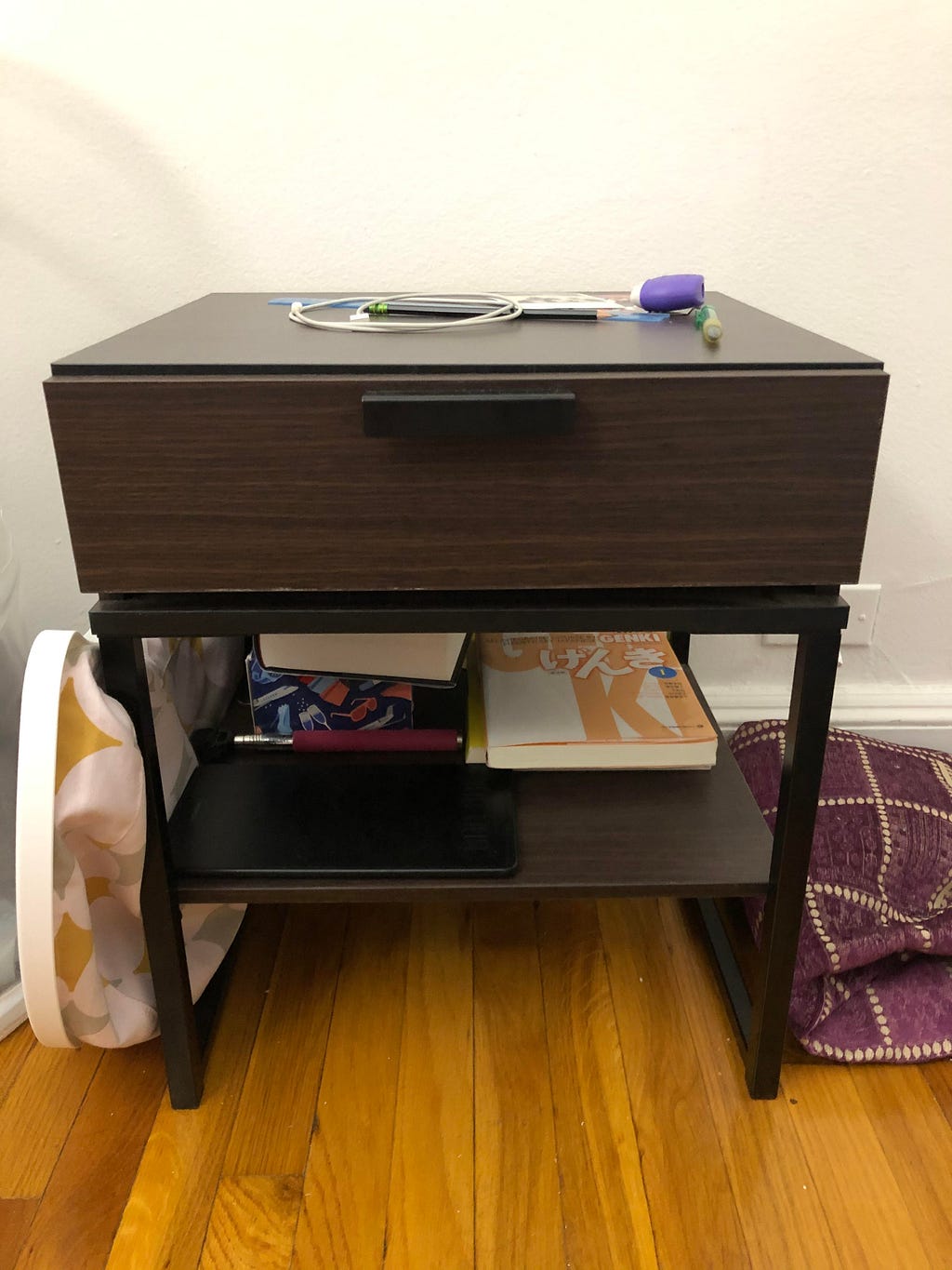 A dark brown wooden nightstand. It has a drawer on top and a space underneath, where the owned has stashed a few books.