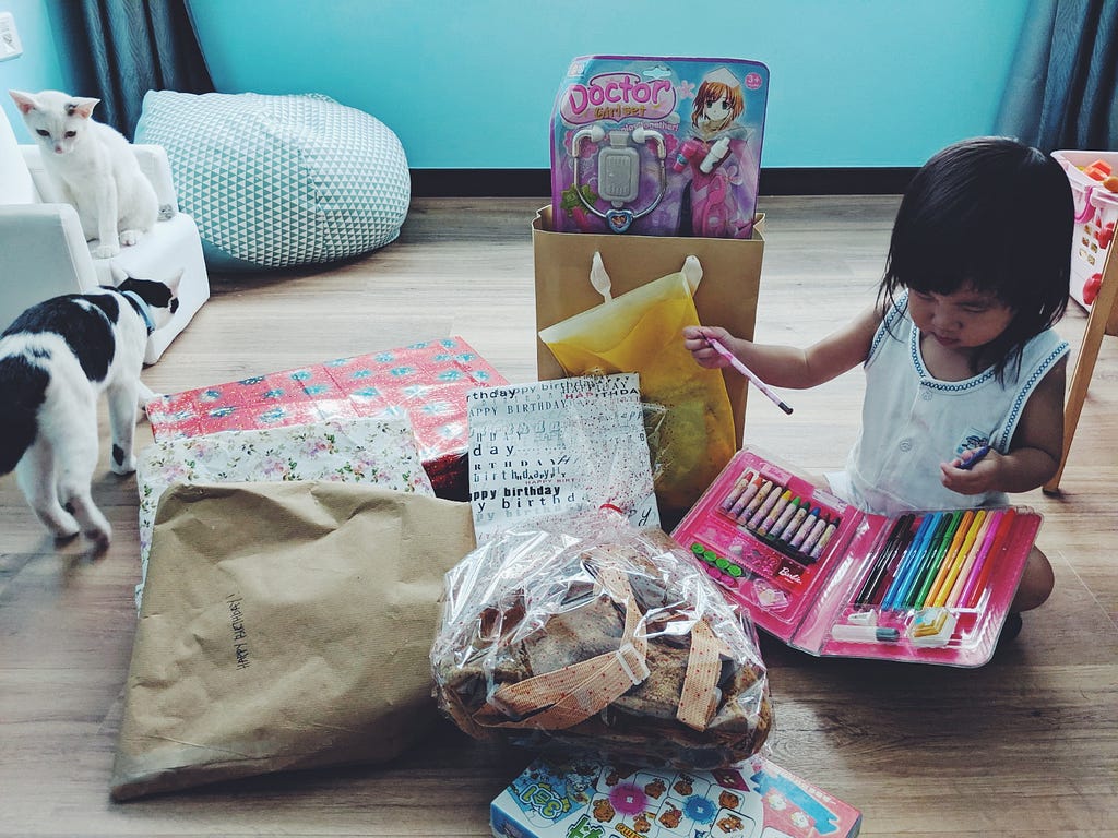 A little girl opening birthday presents, surrounded by two cats