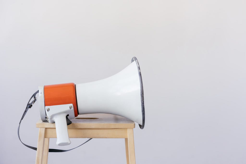 An orange and white megaphone sits idle on a wooden stool