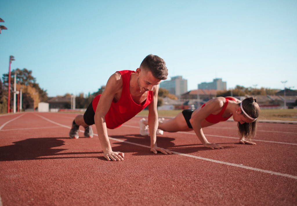 A man and woman doing push-ups on an outdoor running track.