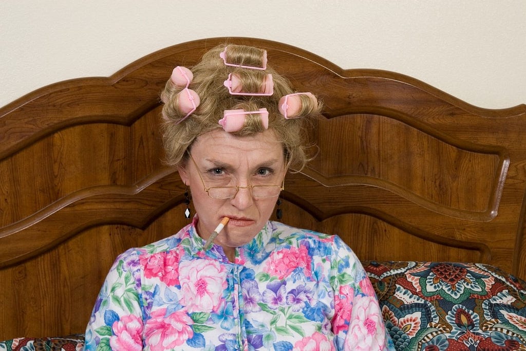 Grandma sitting in bed with rollers in her hair and a grumpy face.
