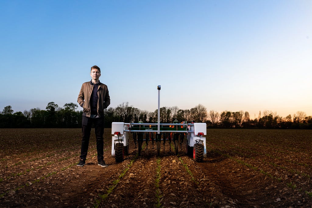 An engineer standing next to an automated agricultural robot in a field.