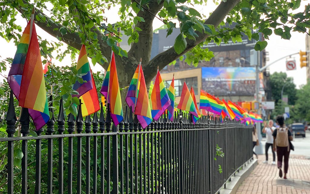 Small rainbow Pride flags line an iron fence at the Stonewall Monument in New York City
