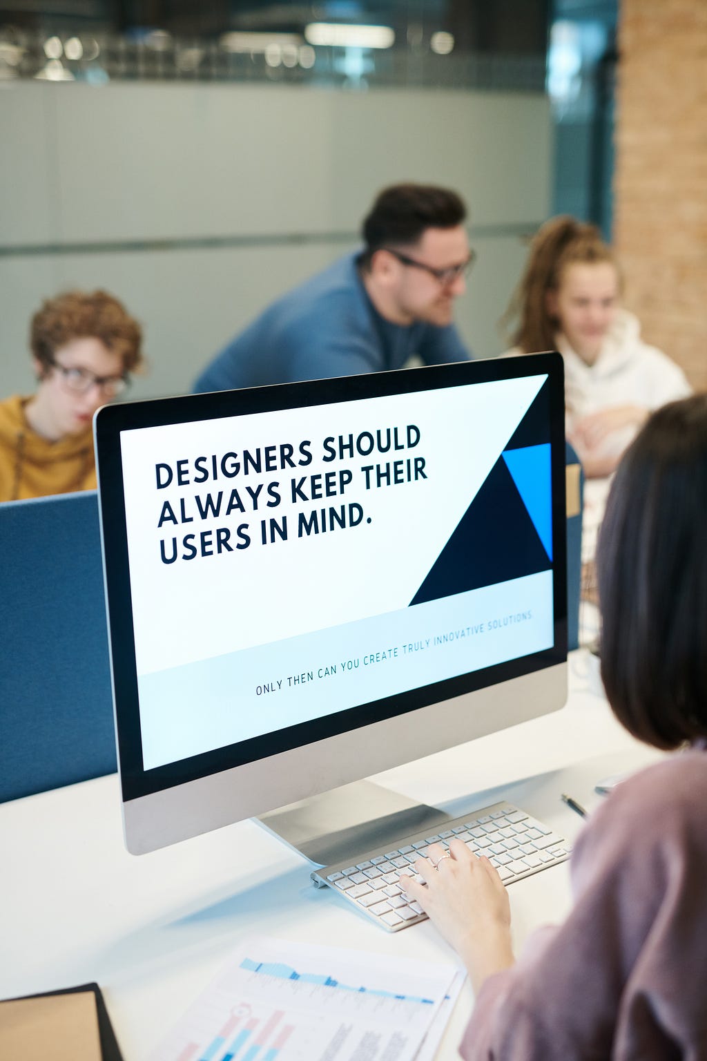A woman looking at a computer screen that reads, “designers should always keep their users in mind”.