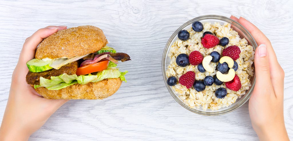 Image of one hand holding a burger and the other hand holding oatmeal with berries