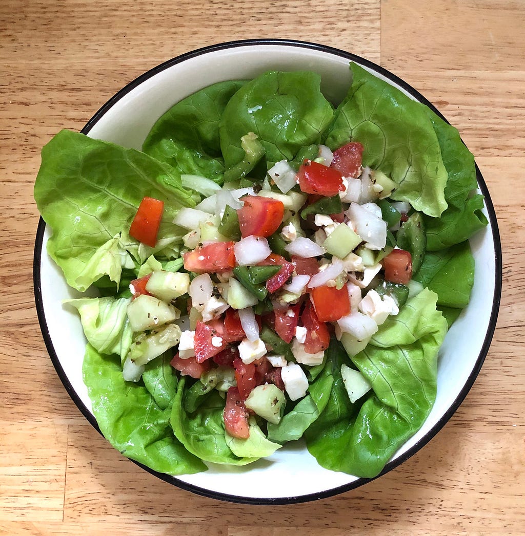 A bowl of green salad with butter lettuce, diced white onions, tomatoes, green peppers, and cucumbers.