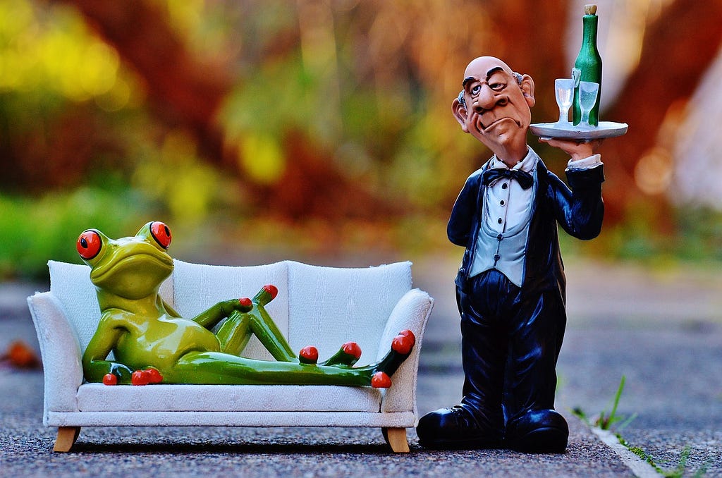 Toys display a scene where a waiter serves a frog lying on a couch.