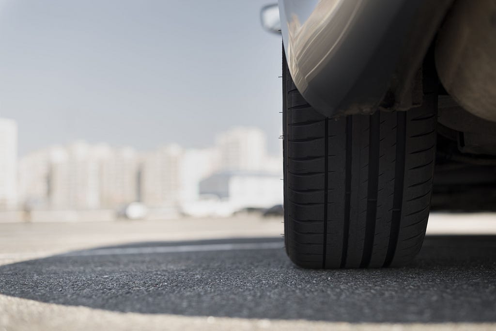 A car, showing its tire, in a city landscape.