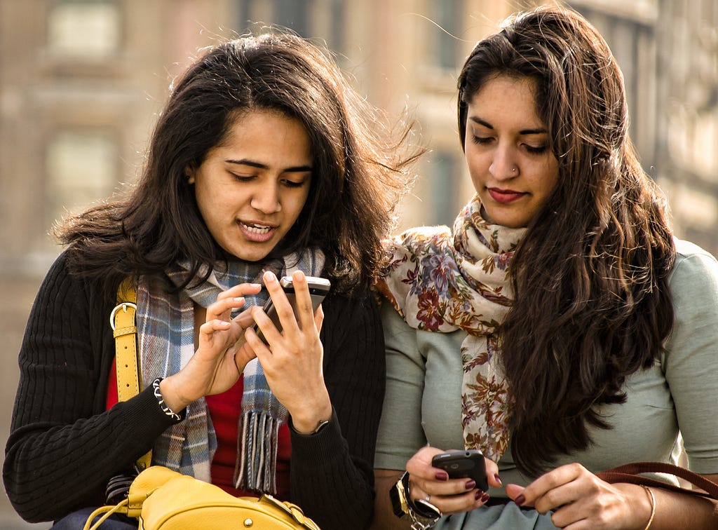 Two women talking while one of them writes a text message on her phone.