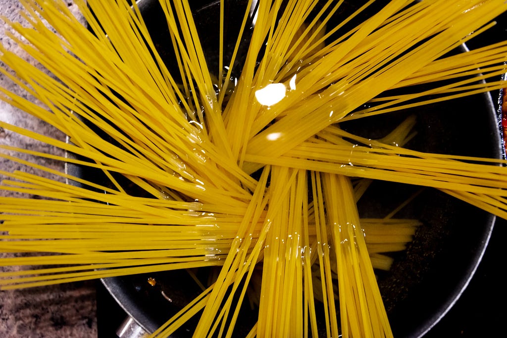 An overhead view of uncooked spaghetti in a pot of water.