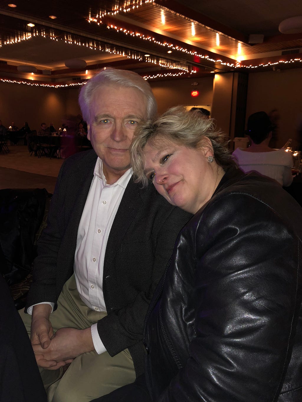 An image of my father David in a suit sitting at an event next to my mother Lori in a black jacket.