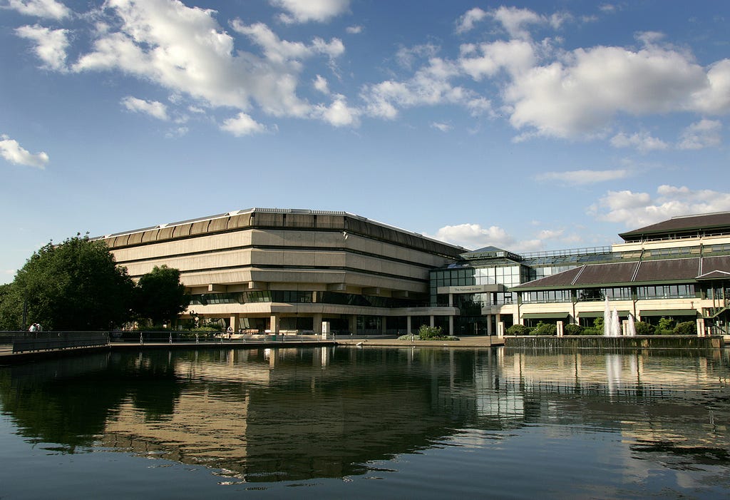 A photograph of The National Archives building under blue skies, reflected in pond, taken at Kew in London, UK.