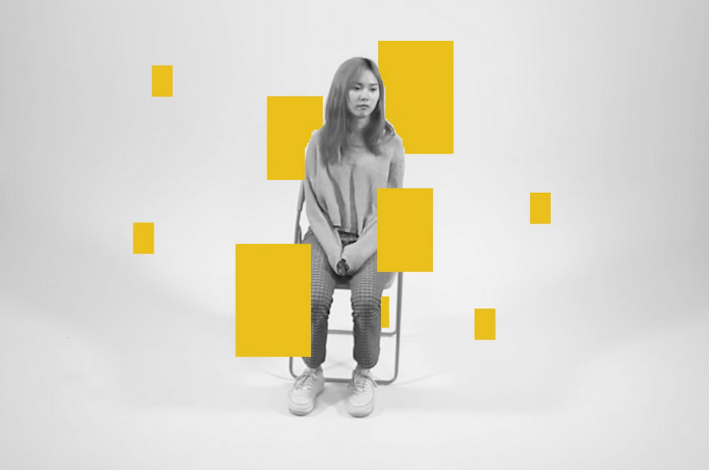 The image shows a person sitting on a chair in a minimalistic setting. Yellow rectangular shapes are superimposed over the person, creating a digital or abstract visual effect.