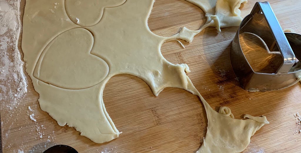 rolled dough rolled out on a wood cutting board with heart shaped cutouts and a heart-shaped cookie cutter.