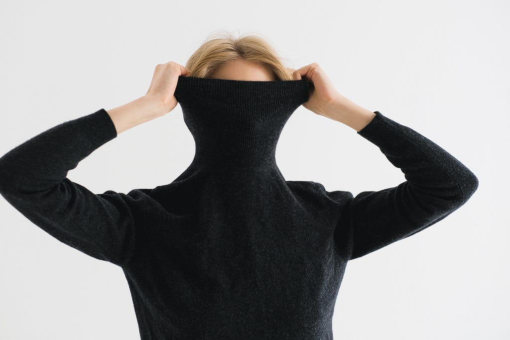 a woman covering her face with the neck of a black turtleneck top
