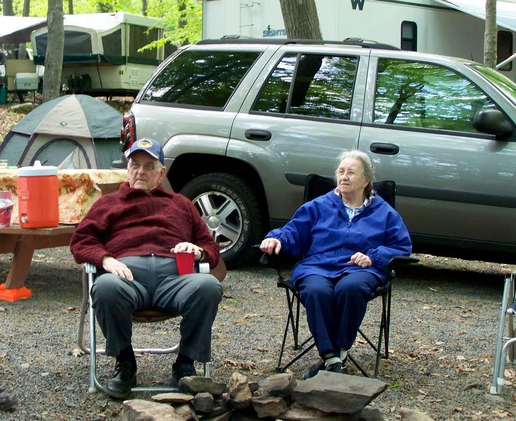 Grammy and Grandpop sitting at their campsite in camping chairs.