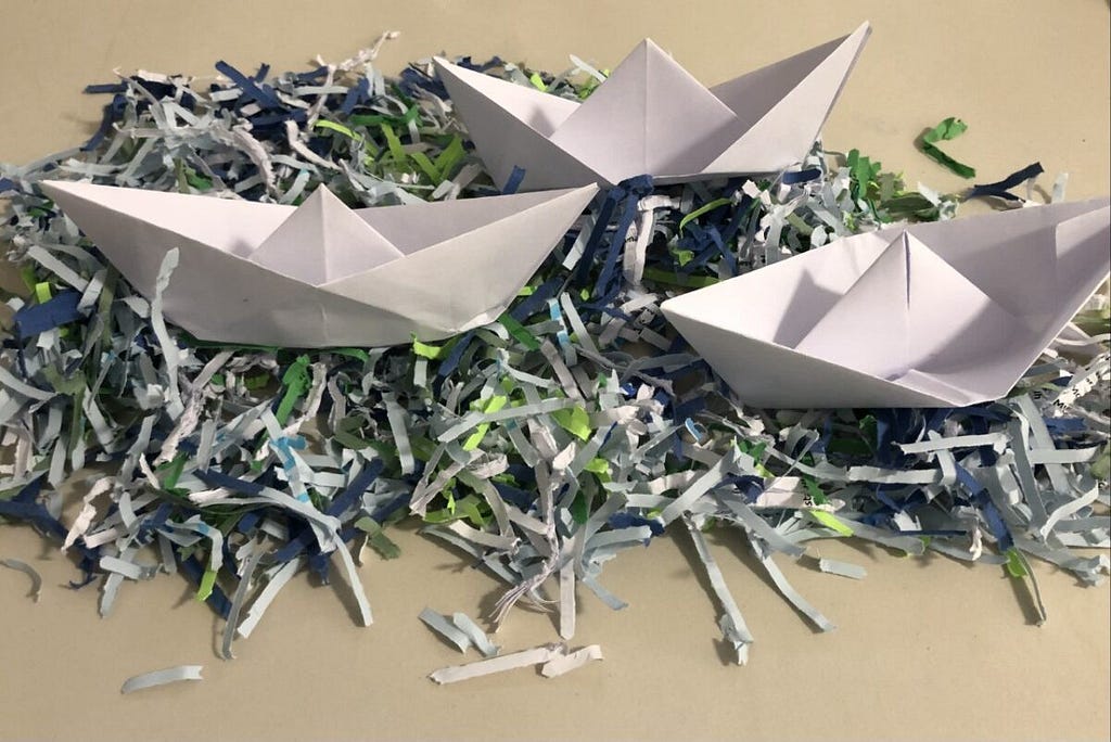 Three paper boats on top of a pile of shredded paper.
