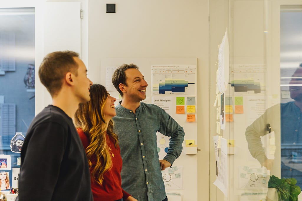 Two men and a woman look happily at the wall hung with concepts