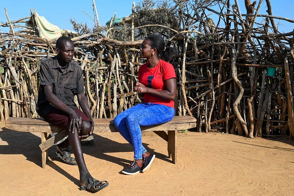 Eli sits in the courtyard in front of his home with Deborah, a local Compassions staff.