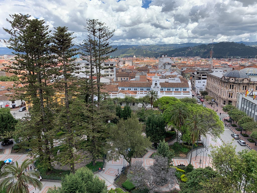 Birdseye view of Park Calderon. A variety of trees are nestles between a city square in Cuenca. Mountains are in the distance