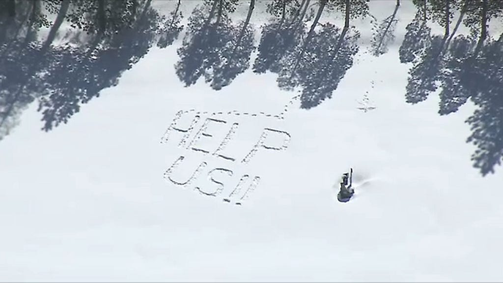 Aerial view of a message written in the snow in Crestline California that reads Help Us!!