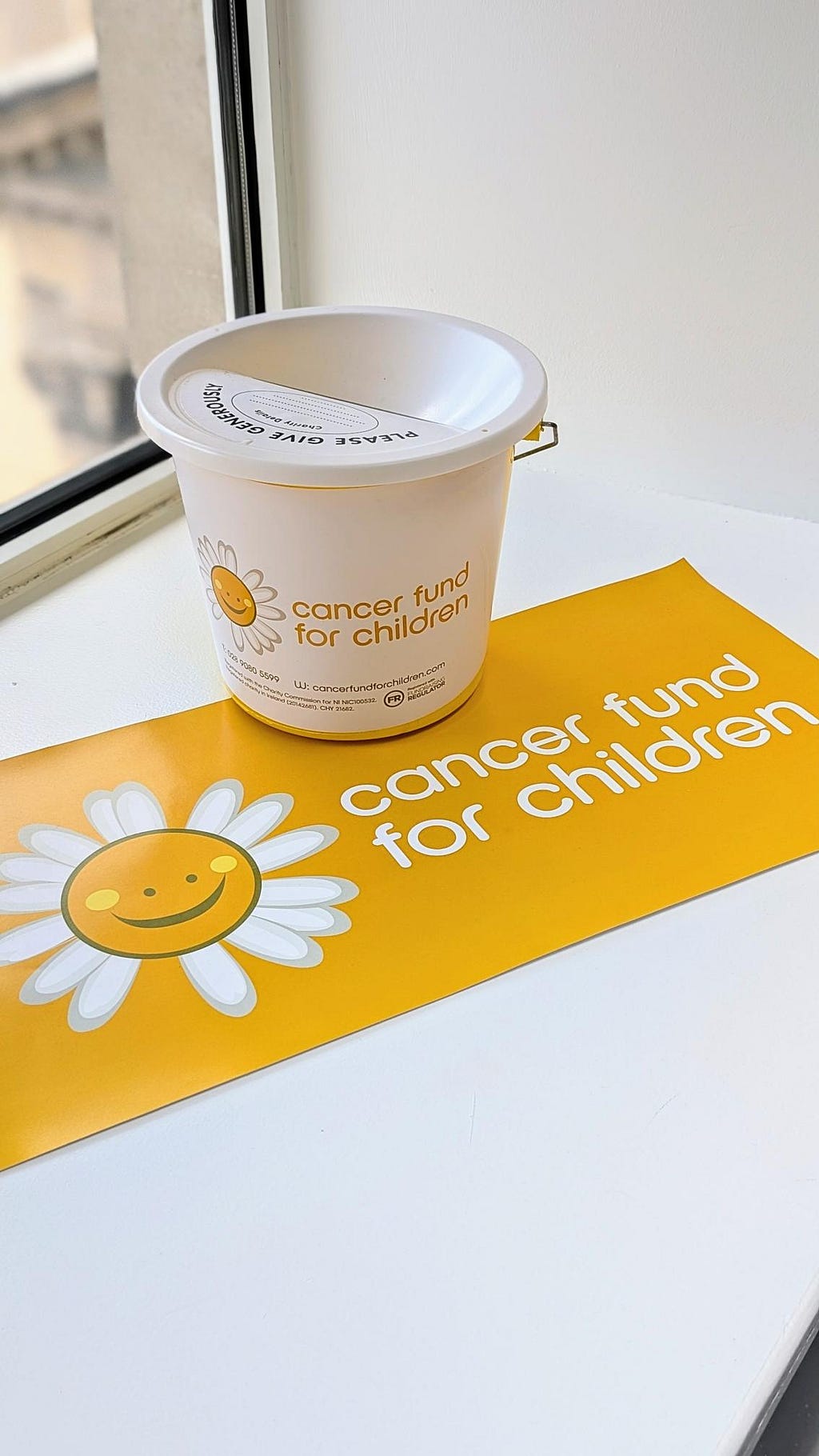 Image of a bucket and poster with a white and yellow Cancer Fund For Children logo