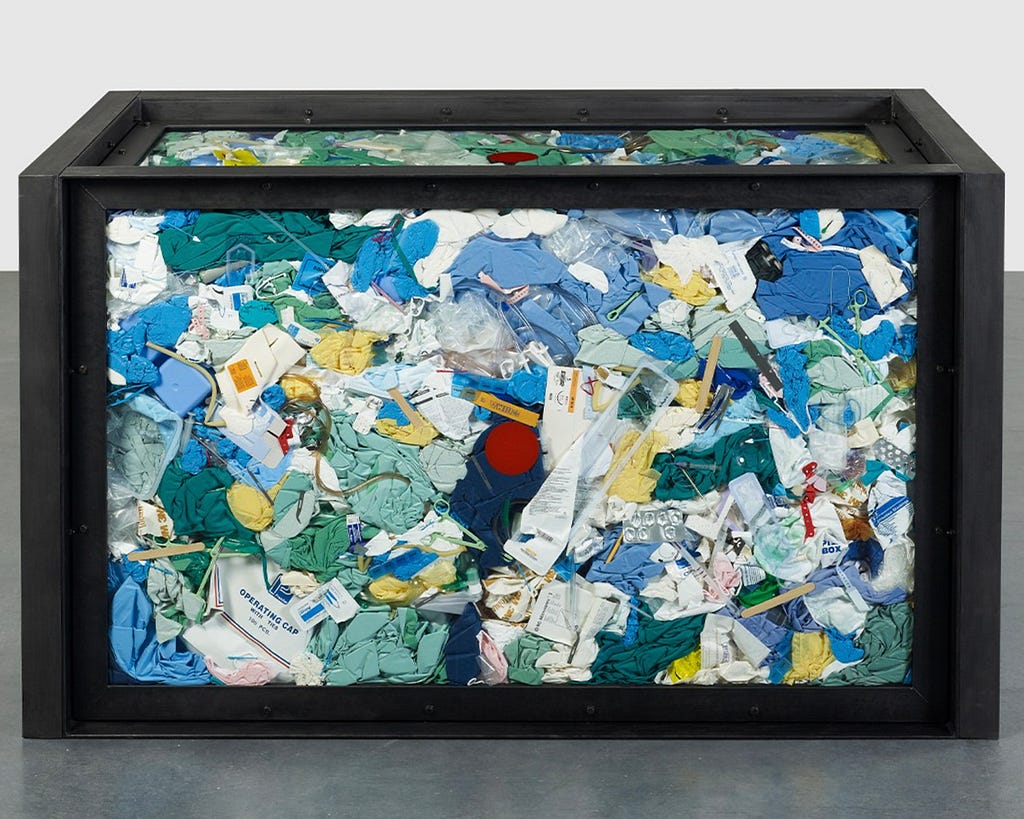 A glass container filled with various medical waste; gloves, syringes etc.