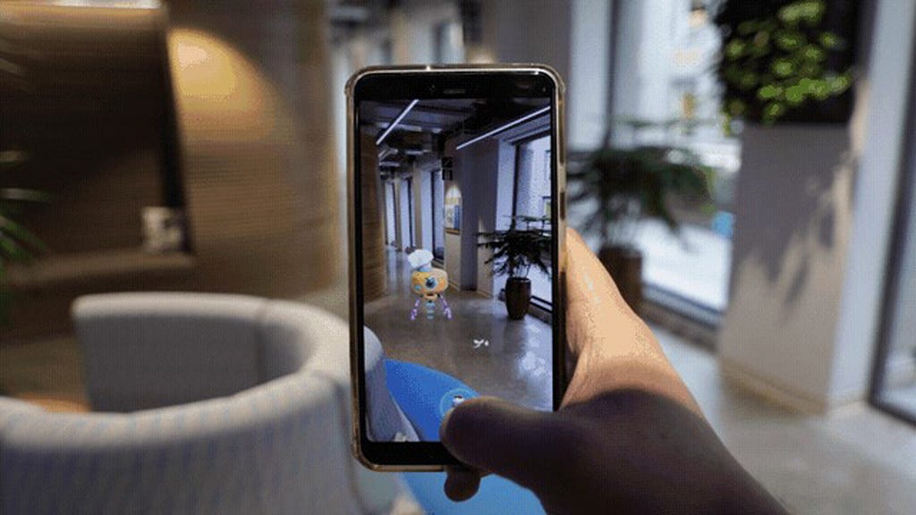 A hand holding up a smartphone, on which a digital character is seen in augmented reality
