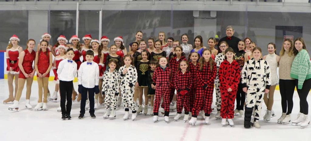 Photo of the participants of the “Polar Express” ice skating show. They are all wearing a variety of Christmas-themed costumes such as Santa hats or red and black checkered pajamas.