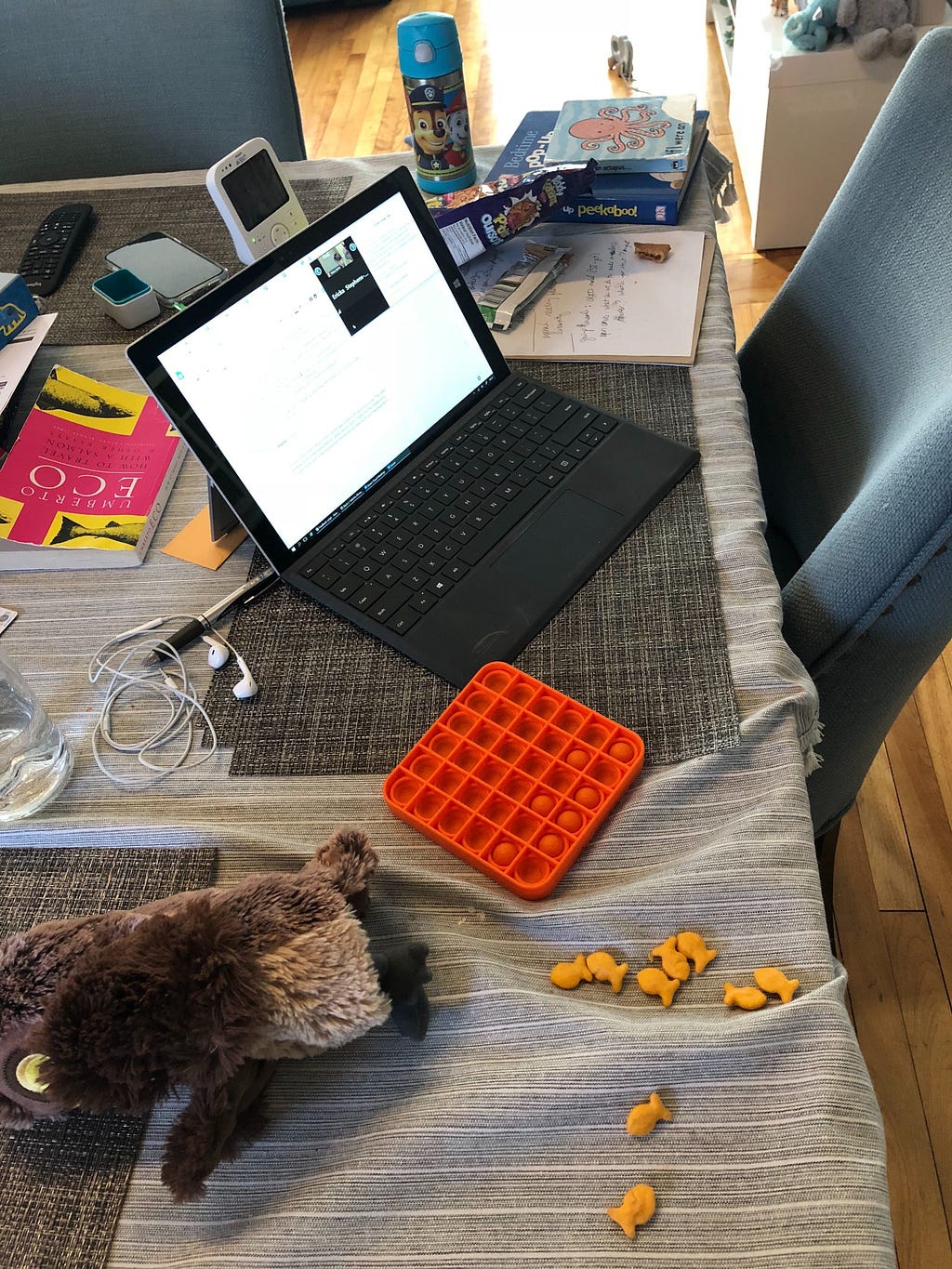 Photo of a work tablet surrounded by children’s toys, books, goldfish crackers, & teddy grahams.