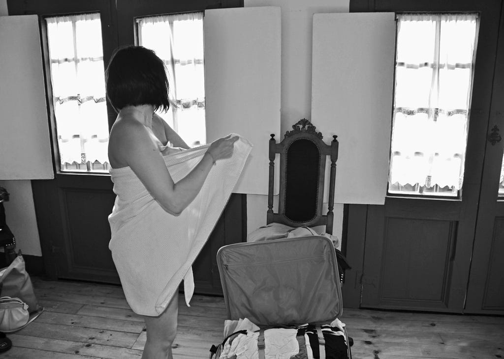 black & white photo of a woman wrapped in a towel standing over an open suitcase