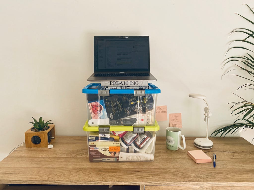 A desk with 2 plastic containers one on top of the other. A laptop on top of the containers to emulate a higher desk.