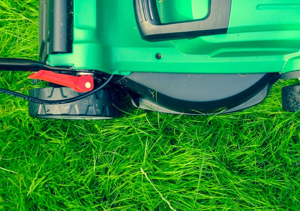 A green lawnmower over a lush lawn of grass.