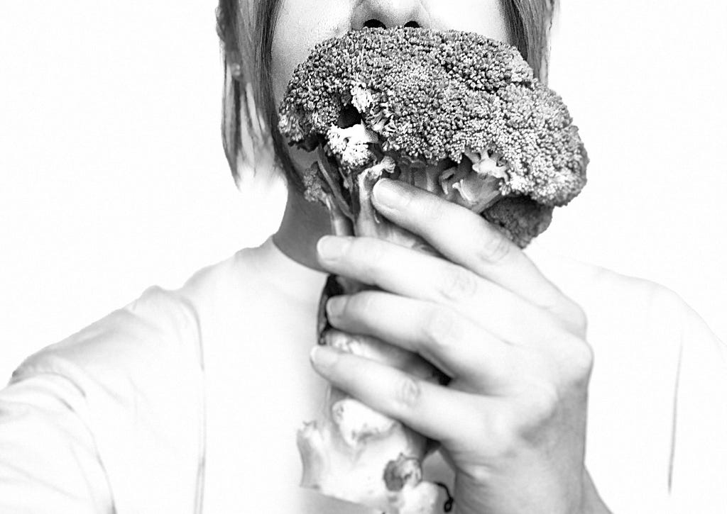 A girl holding a broccoli in front of her face
