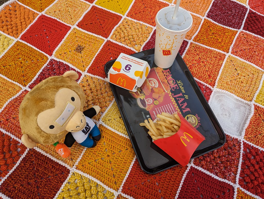 Sauce Monkey plush is to the left of the food tray. A pack of 6 McNuggets, McDonald’s fries, and a drink sits on the tray.